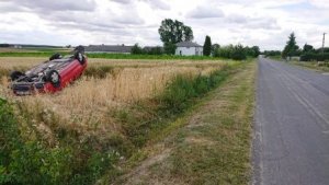 Wywrócony kołami do góry samochód osobowy, w zbożu około 8 metrów od drogi