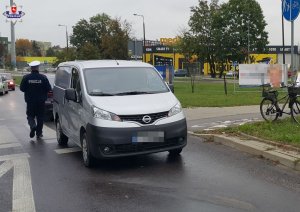 samochód stojący na ulicy a przy nim policjant w białej czapce