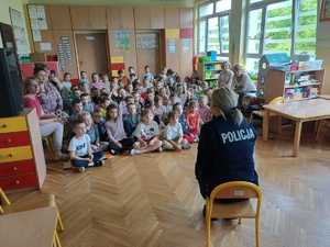 policjantka siedzi przodem do dzieci siedzących na podłodze